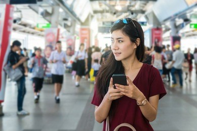asian woman passenger with casual suit using the smart mobile phone in the train rails or subway for travel in the big city, lifestyle and transportation concept
