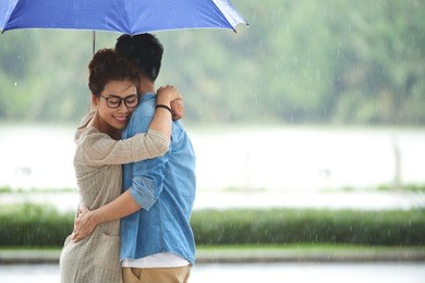 portrait of loving asian couple embracing under umbrella on date in rain, copy space