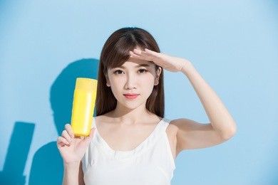 woman holding sunscreen and looking somewhere on blue background