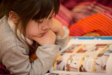 young japanese girl reading a coming book on her bed.