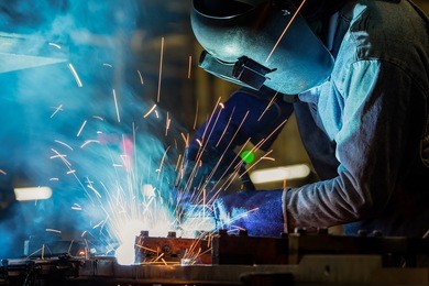 industrial worker is welding metal part in factory