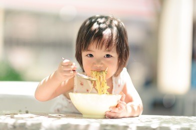 2-3 years old asian girl eating noodles alone. she wear a white dress and looked at the camera. practice discipline for children from childhood to the children themselves.