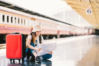 asian backpack traveler woman using generic local map, siting alone at train station platform with luggage. summer holiday traveling or young tourist concept