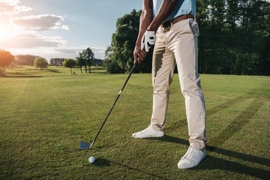 cropped shot of golfer holding club and hitting ball on green grass