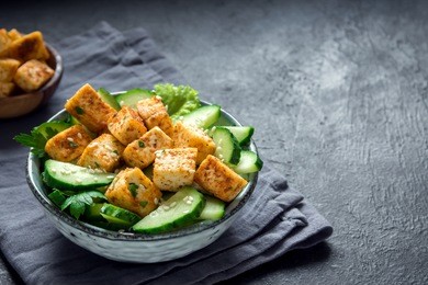 fried tofu salad with cucumbers and sesame seeds. homemade asian vegetable and tofu salad in ceramic bowl on black stone background. healthy asian diet vegan vegetarian salad food.