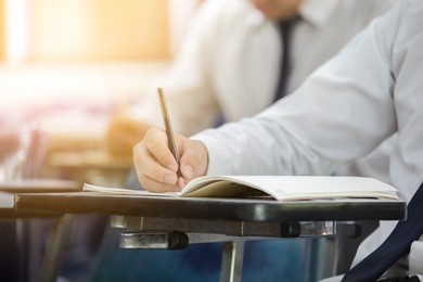 side view.university or high school student holding pencil.sitting on row chair writing final exam in examination room or study in classroom.student in uniform.space for text.