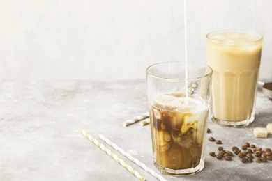 milk pouring in ice coffee in a tall glass on a gray background. copy space. food background