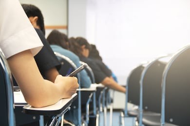 hands university student holding pen writing /calculator doing examination / study or quiz, test from teacher or in large lecture room, students in uniform attending exam classroom educational school.