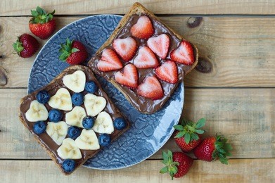 plate with fruit toasts. breakfast sandwiches with chocolate butter, banana slices, strawberry and blueberry. heart shaped fruits. sweet food. fruit snack