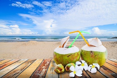 young coconut juiced with plumeria flower on wood floor against blurred beach background. summer holiday concept, 