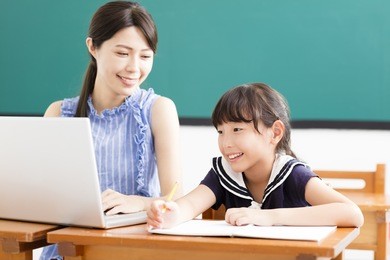 young teacher helping child with computer lesson
