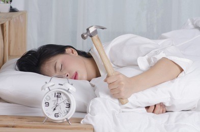 beautiful young woman tries to break the alarm clock with hammer