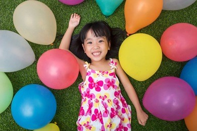 asian little chinese girl lying on the grass amongst colorful balloons at outdoor park