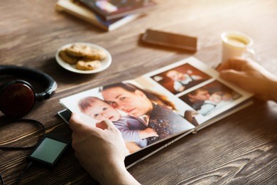 the hand man holding a family photo album  against the background of the a wooden table
