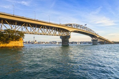 auckland harbour bridge in evening light with yachts passing under.
