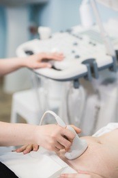 close-up of doctor moving ultrasound probe on pregnant woman's stomach in hospital