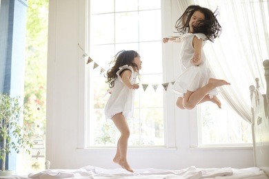 happy family at home. sisters jumping on the bed, playing and laughing