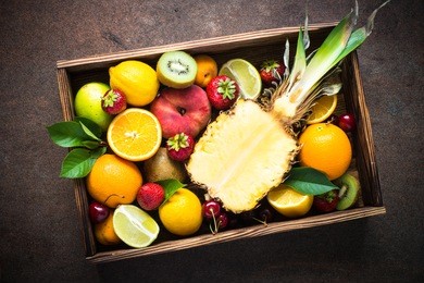 fruit and berries in wooden box over dark stone table. top view with copy space.  pineapple, citrus and berry mix.
