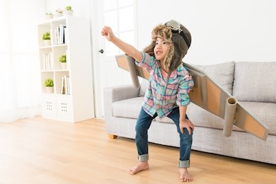 smiling sweet female children wearing astronaut costume making ready to fly gesture standing on living room wooden floor at home.