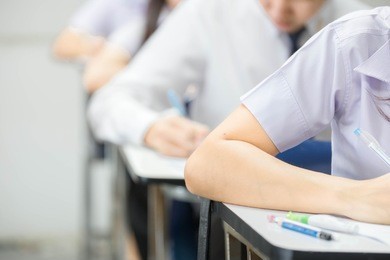 front view.university or high school student sitting on row chair writing final exam in examination room or study in classroom.student in uniform.space for text.education concept