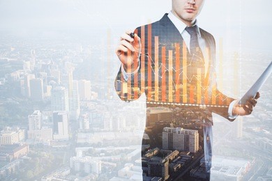 young european businessman with document in hand drawing abstract business chart on city background with copy space. finance concept. double exposure