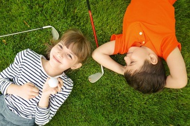 cute children with ball and drivers lying on golf course