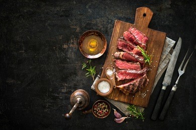 sliced medium rare grilled beef ribeye steak on cutting board on dark background