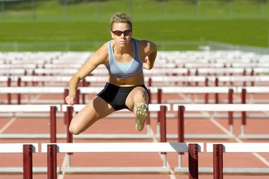 track and field athlete jumps over hurdles.