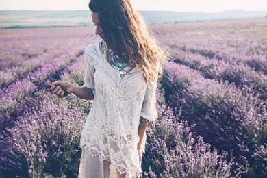 beautiful model walking in spring or summer lavender field in sunrise backlit. boho style clothing and jewelry.