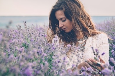 beautiful model walking in spring or summer lavender field in sunrise backlit. boho style clothing and jewelry.
