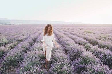 beautiful model walking in spring or summer lavender field in sunrise backlit. boho style clothing and jewelry.