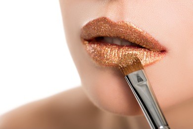 close up view of woman applying golden lipstick with makeup brush isolated on white