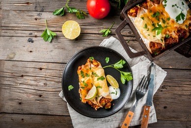 mexican food. cuisine of south america. traditional dish of spicy beef enchiladas with corn, beans, tomato. on a baking tray, on old rustic wooden background. copy space top view.