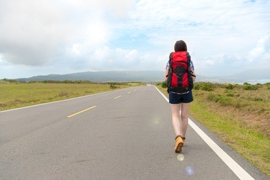 beautiful elegant traveler carrying backpack walking on country road. back view photo.