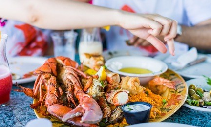 closeup of lobsters and seafood on plate with hand reaching for garlic butter