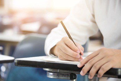 closeup hand.university or high school student holding pencil.sitting on row chair writing final exam in examination room or study in classroom.student in uniform.space for text.education concept