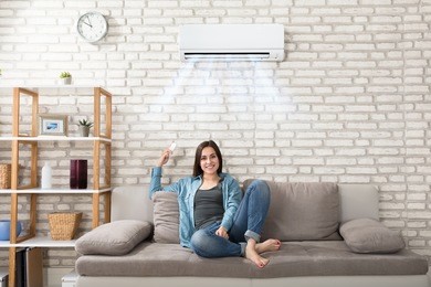 happy young woman holding remote control relaxing under the air conditioner
