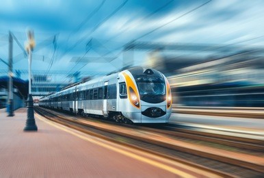 high speed train at the railway station at sunset in europe. modern intercity train on railway platform. urban view with beautiful passenger train on railroad and buildings. railway transportation