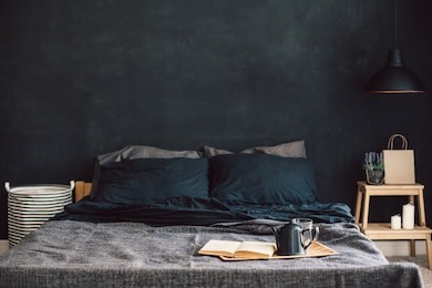 black stylish loft bedroom. unmade bed with breakfast and reading on tray. lamp and interior decor over blank blackboard wall with copyspace. cozy modern living space.