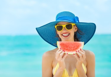 woman relaxing on the beach on a summer day smiling with a slice of watermelon in her hand.