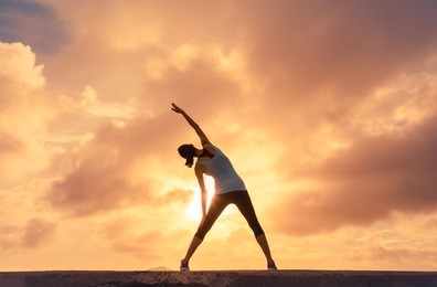 woman doing stretching warm up exercise outdoors against a beautiful sunset. 