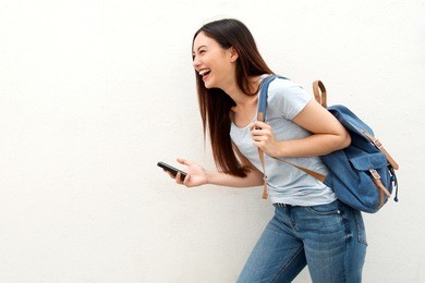 portrait of laughing woman holding mobile phone and backpack
