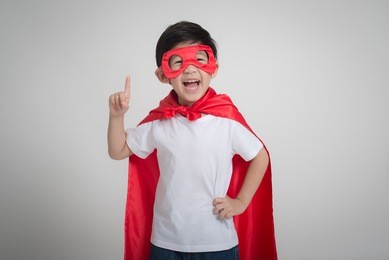 portrait of asian child in superhero's costume pointing up on gray background