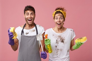 amazed female and male with dirty clothes and faces being pleasantly surprised to finish work very quickly. cheerful woman holding sponge and washing spray and her husband with brush and sponge