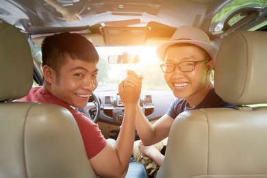 group portrait of joyful vietnamese friends looking at camera with wide smiles and giving high five while sitting in car ready for unforgettable road trip, lens flare