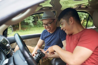 smiling handsome men sitting together in car and looking through pictures on professional camera