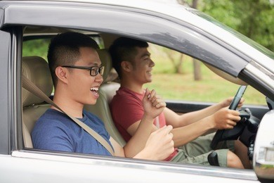 profile view of two cheerful asian friends chatting animatedly with each other during long-awaited road trip
