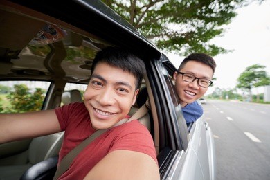 waist-up portrait of handsome vietnamese man taking selfie with best friend while driving car