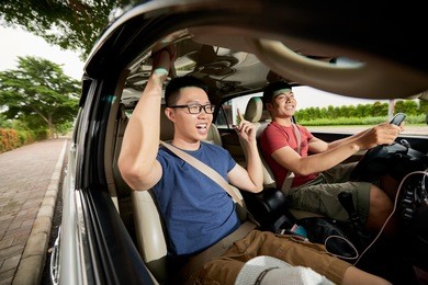 joyful vietnamese man with toothy smile enjoying road trip with best friend while driving car