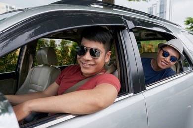 group portrait of joyful friends with toothy smiles wearing eyeglasses sitting in car and anticipating road trip
